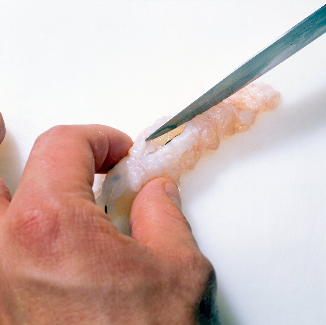 Close-up of hand cutting shrimp from back to expose intestines, step 6
