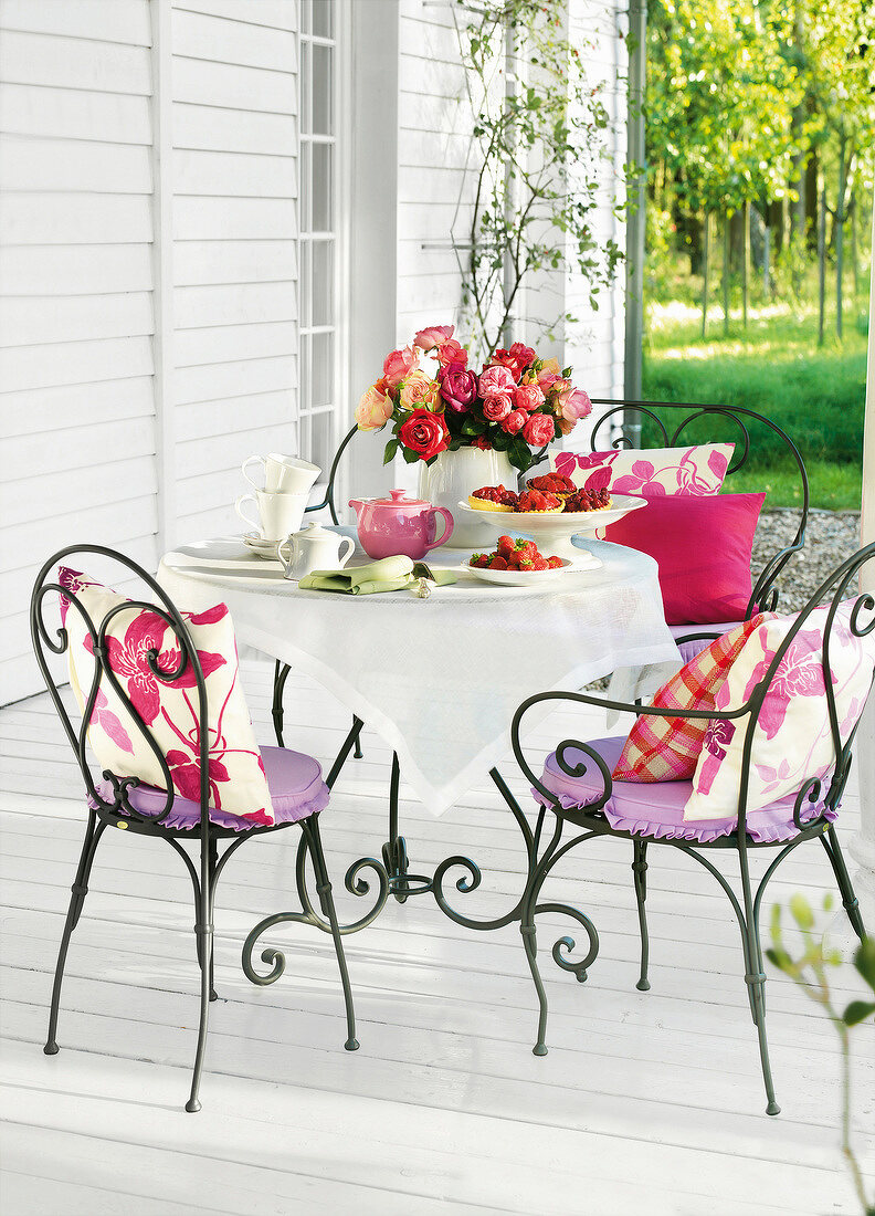 Iron chairs and table laid with strawberry tarts and rose vase on terrace
