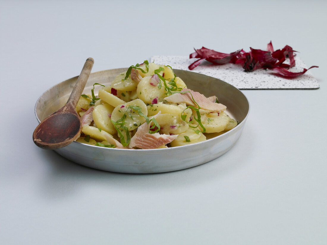 Wild garlic potato salad with smoked fish and red onions in serving dish