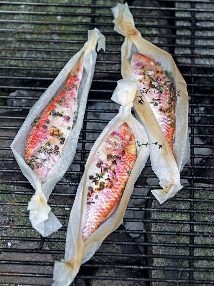 Three mullet fish with capers and thyme in packets on grill