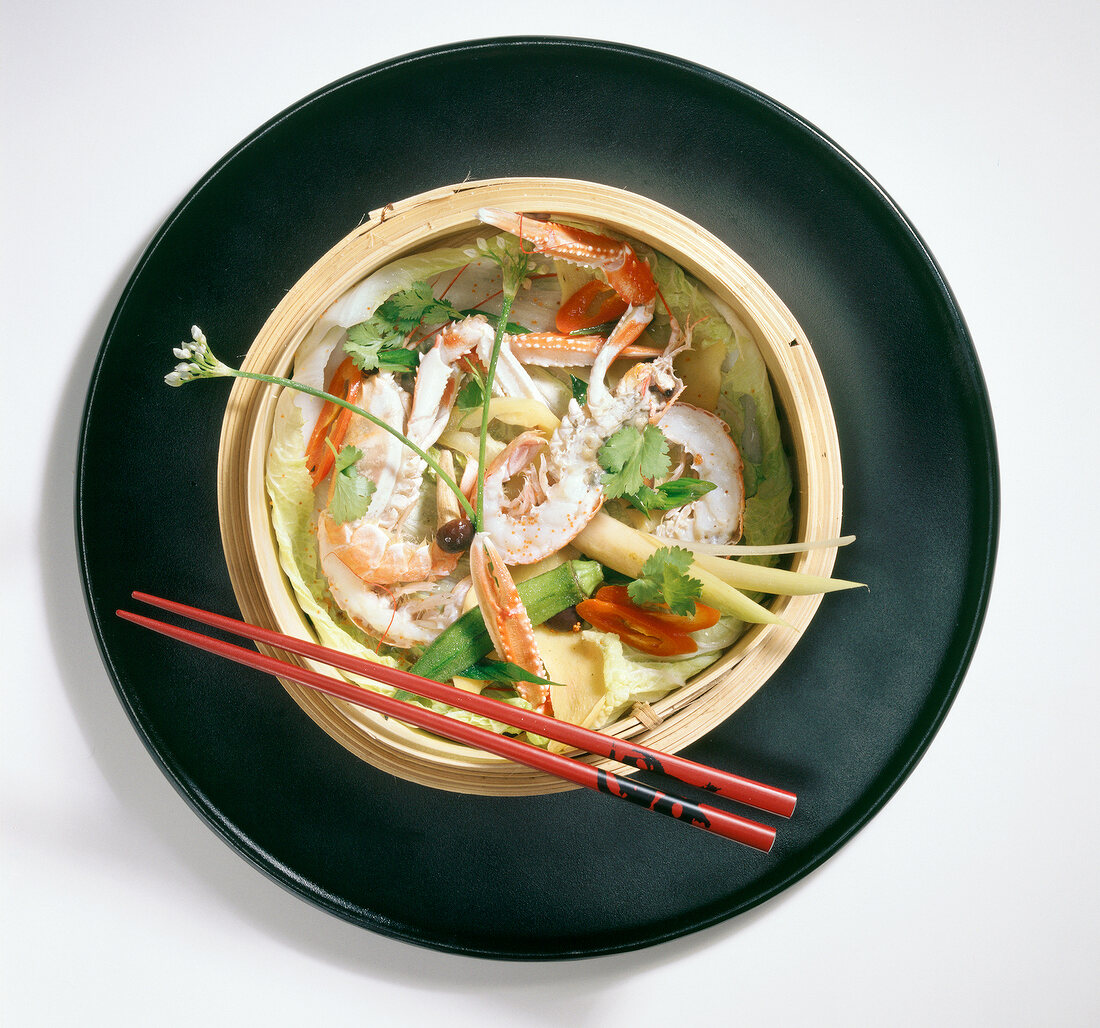 Steamed shrimp with vegetables and ginger slices on plate with chopsticks