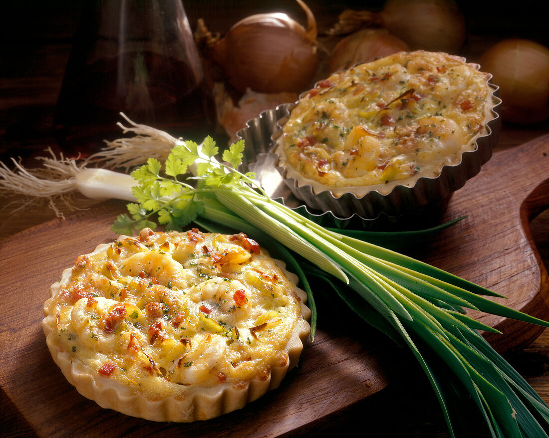 Two small leek quiche with shrimp in baking dish and scallions on wooden board