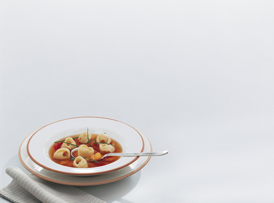 Tortellini in beef broth on plate on white background
