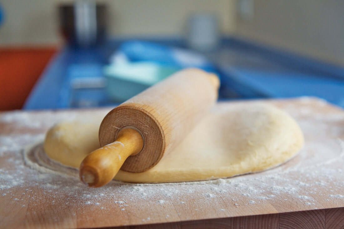 Flour dough is rolled out flat with rolling pin on wooden board
