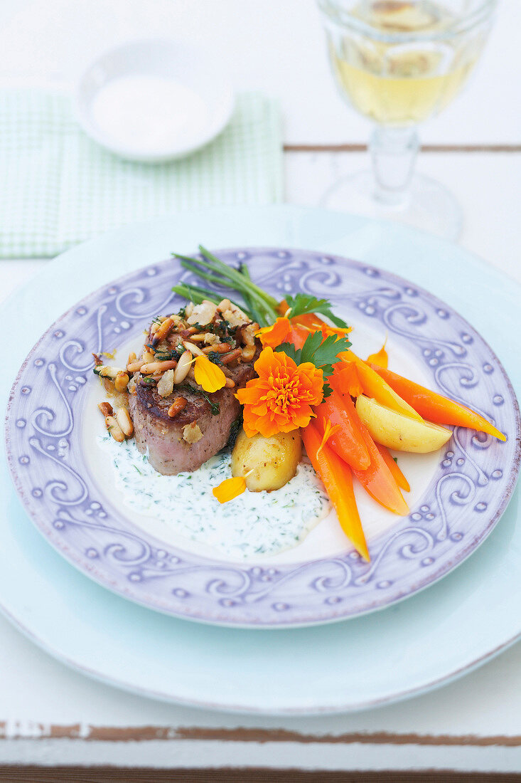 Veal medallions with pine nuts, herbs, potatoes and carrots served on plate