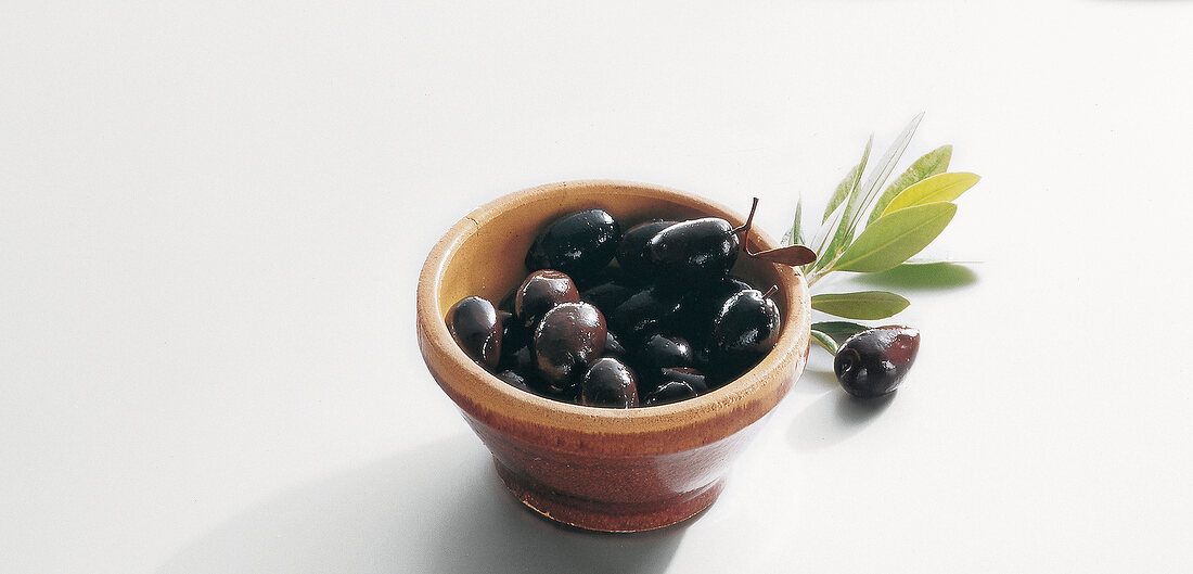 Black olives in bowl on white background