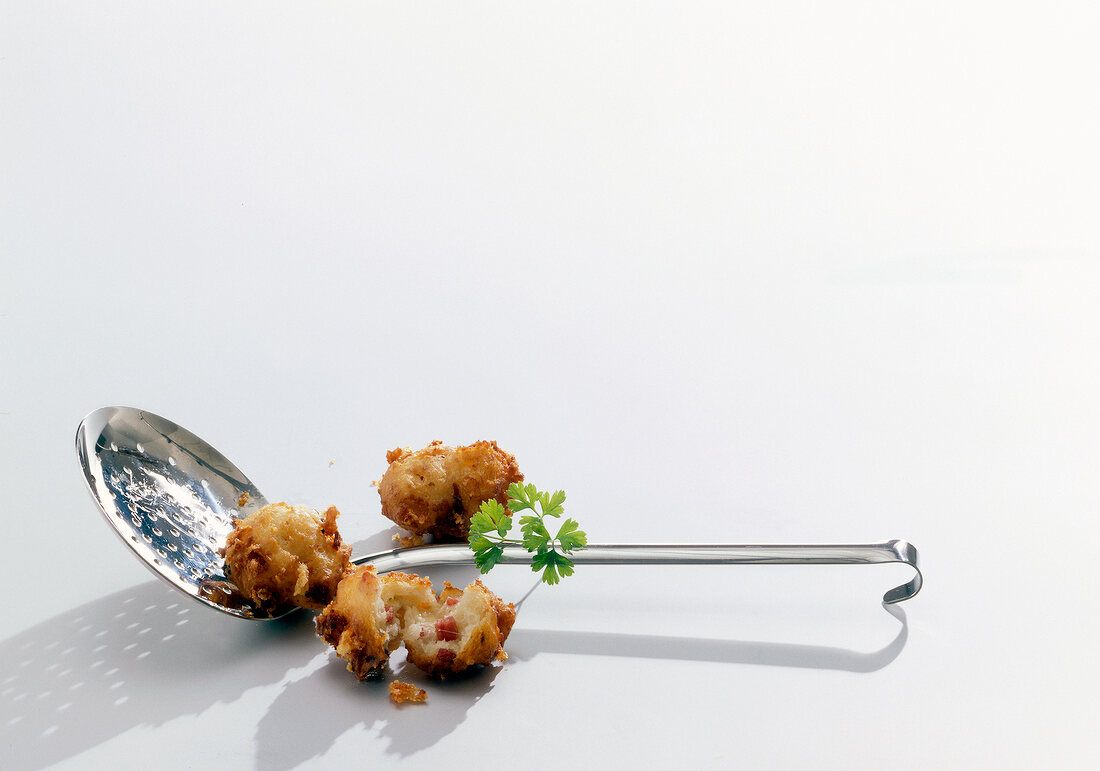 Close-up of fried potato balls on ladle against white background