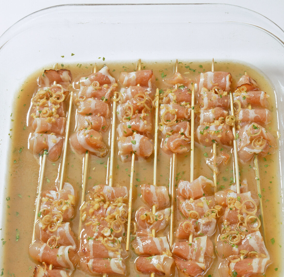Close-up of marinated chicken and bacon skewers in tray