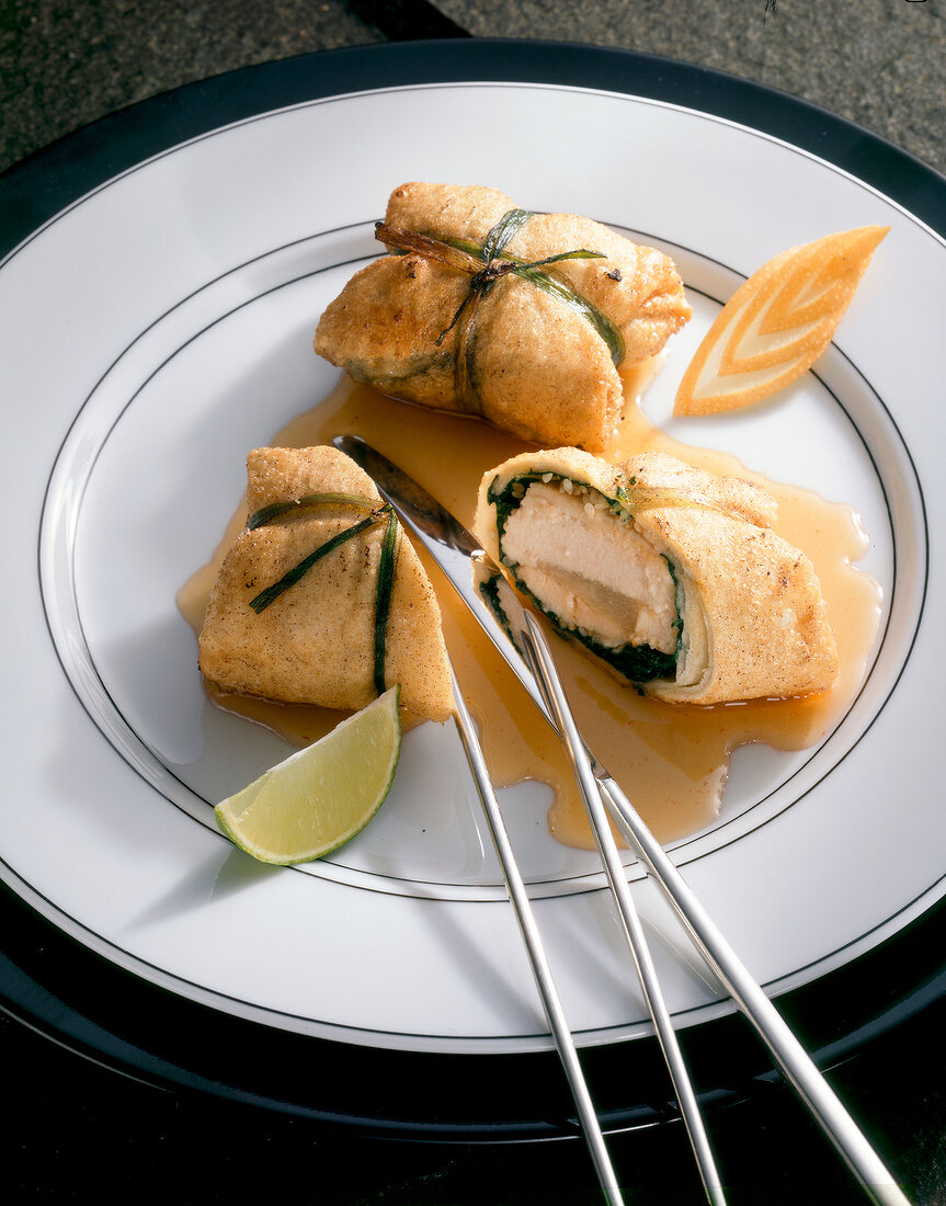 Close-up of chicken in pastry parcel with chilli sauce and lime on plate