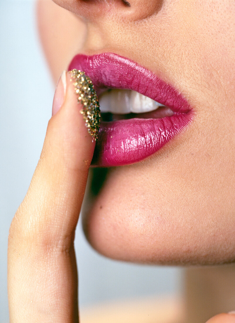 Close-up of woman's lips wearing red lipstick applying golden dust on it with finger