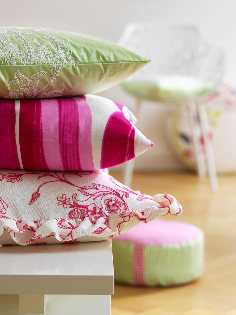 Pink, green and white cushions stacked on table