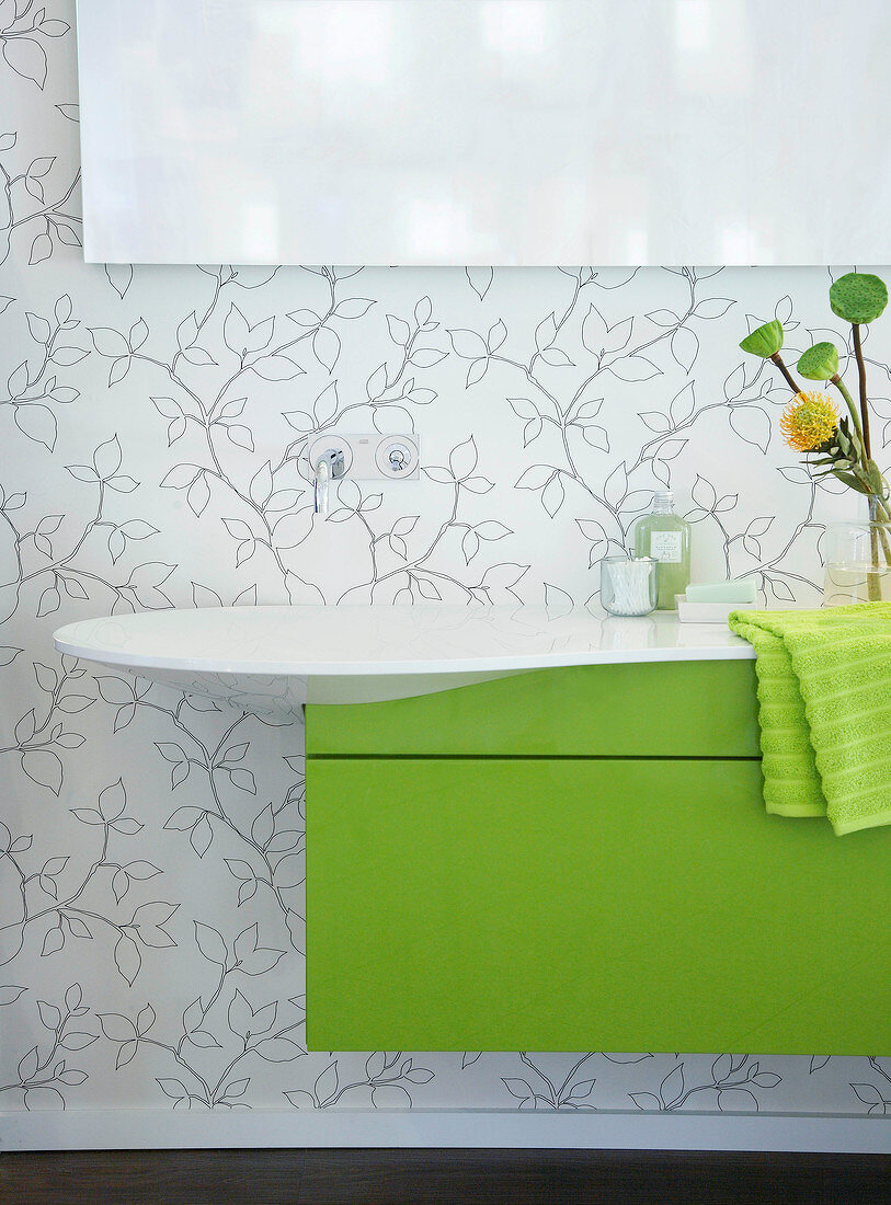 Weißes Waschbecken mit grünem Wascht isch, darüber Spiegel, geblümte Wand