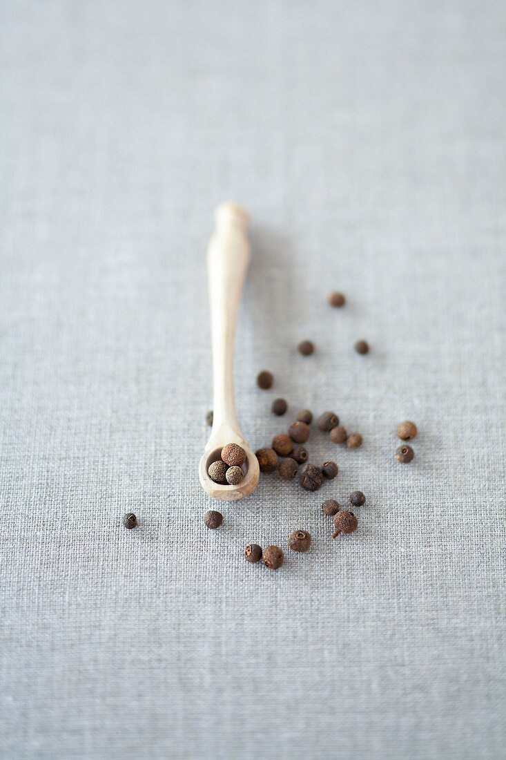 Allspice in small wooden spoon and some spilt on gray surface