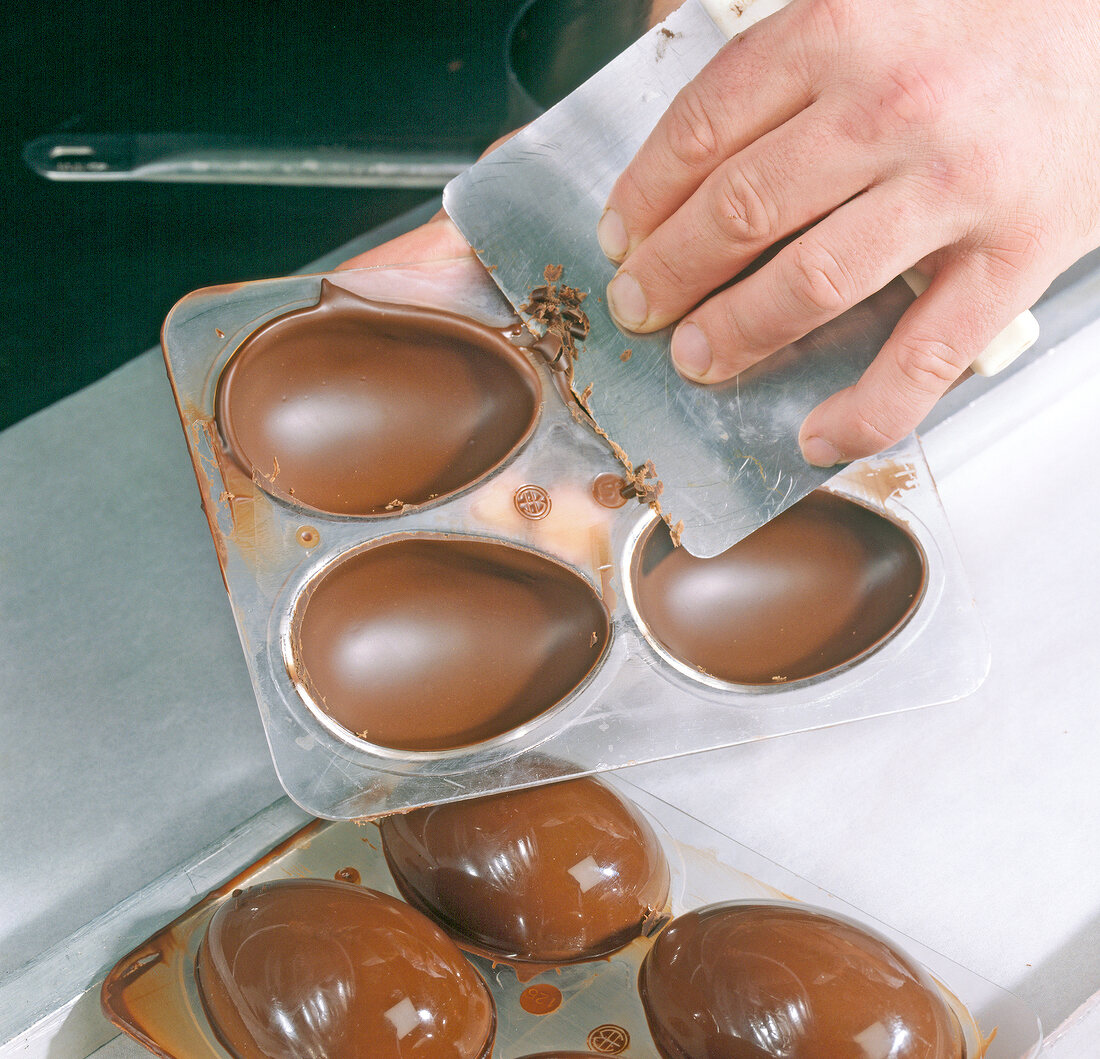 Close-up of hand scraping edges with scraper on egg shape moulds, step 4