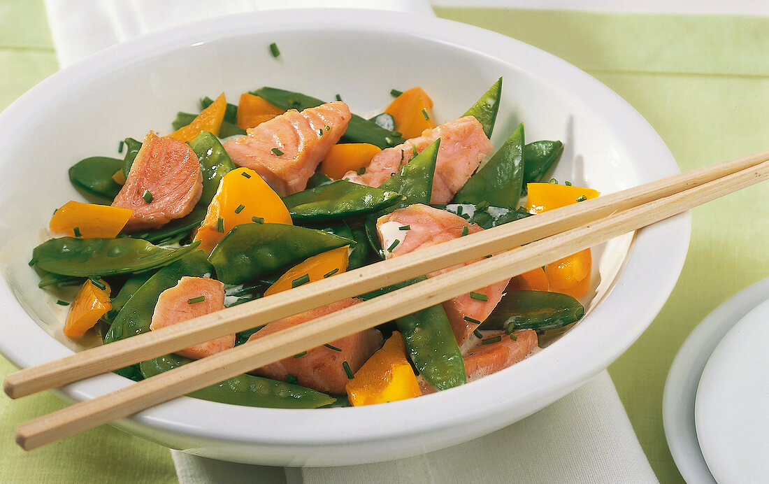 Close-up of bowl of salmon with sugar snap peas, peppers and cheese