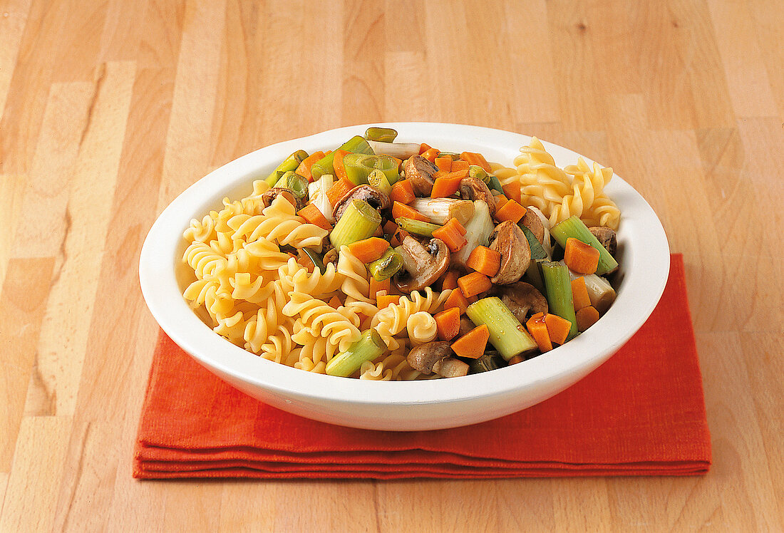 Bowl of fusilli salad with carrots, mushrooms and leeks on orange table mat