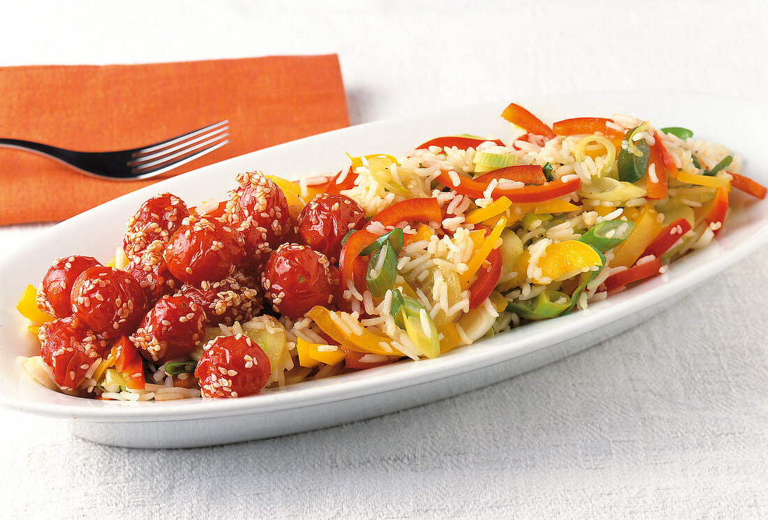 Close-up of rice and vegetable salad with stewed tomatoes and sesame seeds in dish