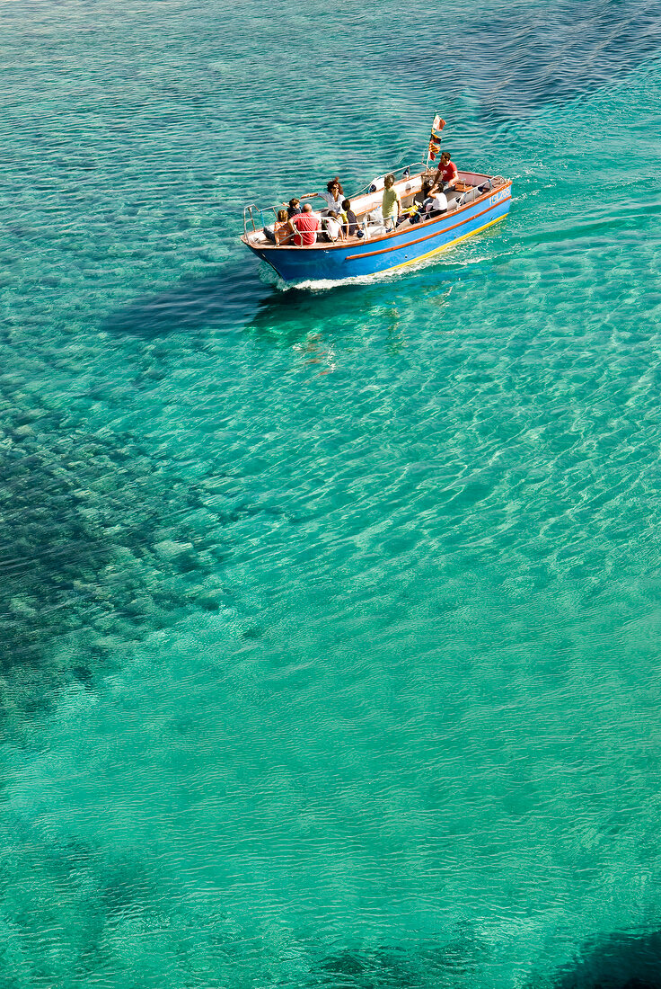 Menschen fahren in einem Boot durchs türkise Wasser, Italien.
