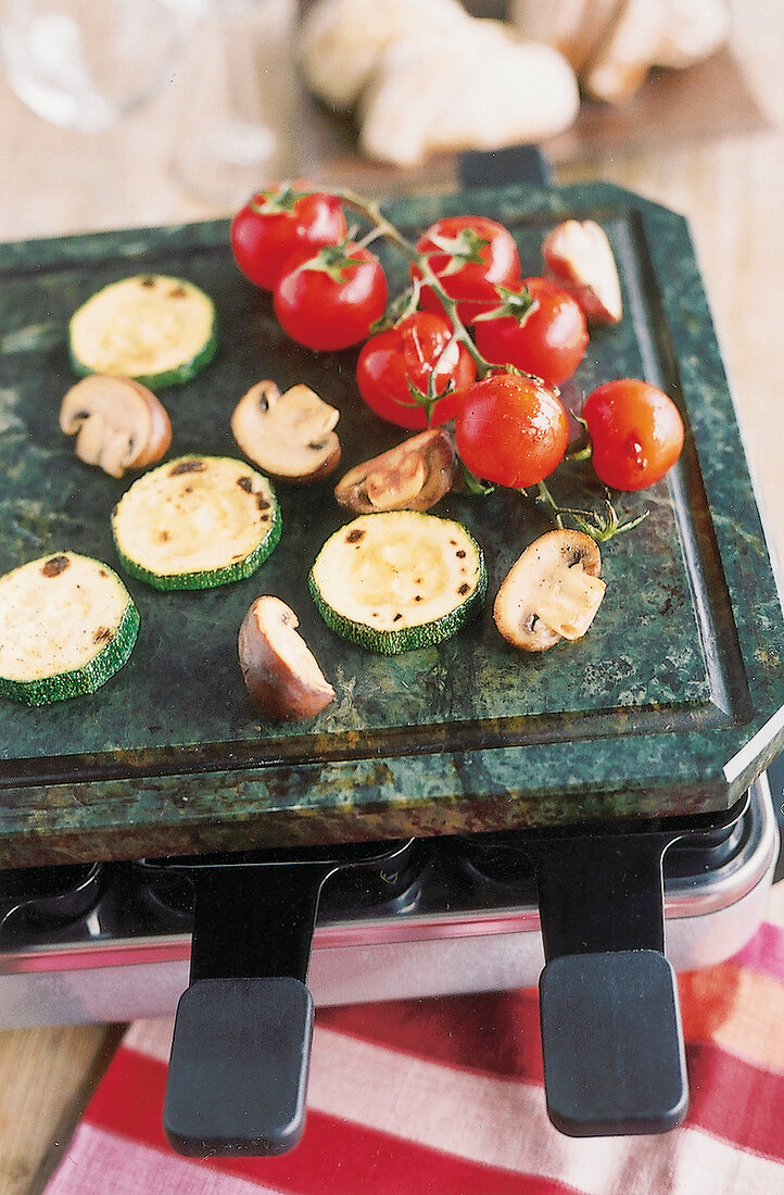 Raclette, Heiße Steinplatte auf Raclettegerät, Zucchini, Tomate