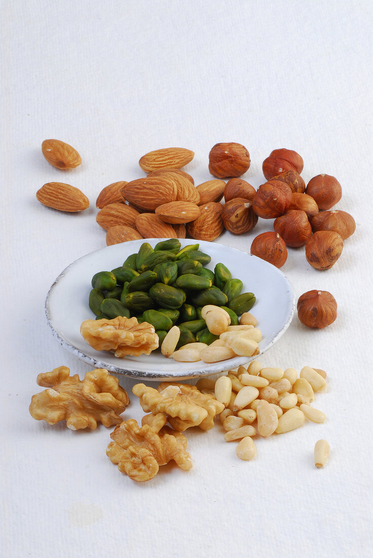 Pistachios, pine nuts, almonds, hazelnuts and walnuts on plate and white background