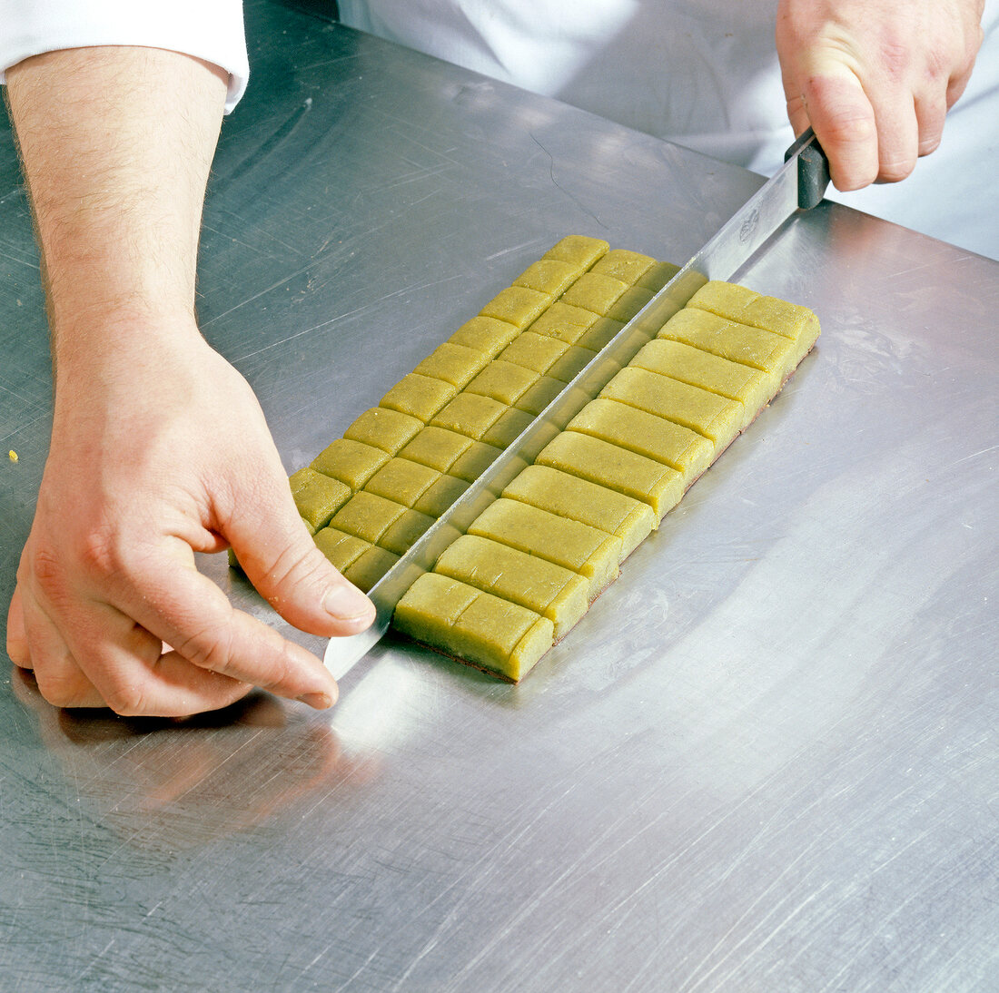 Chef cutting marzipan-pistachio rolled dough into squares, step 6