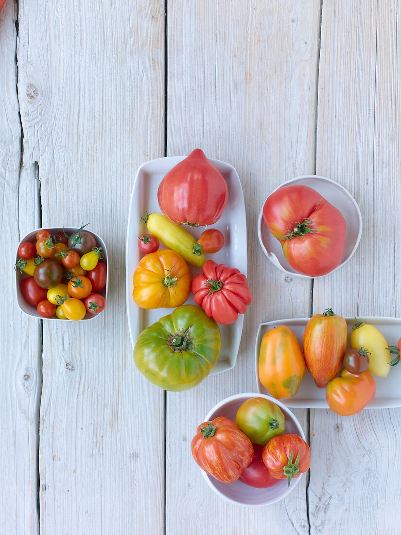 Different kinds of tomatoes in bowls and dishes on wooden table, overhead view