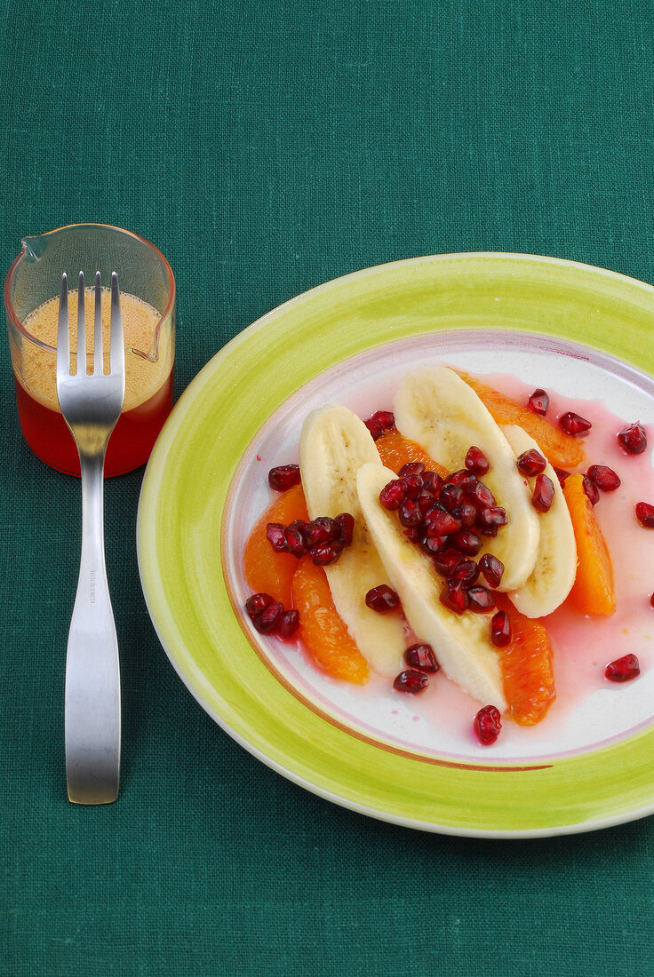 Banana, blood orange and pomegranate seeds on plate besides glass of juice