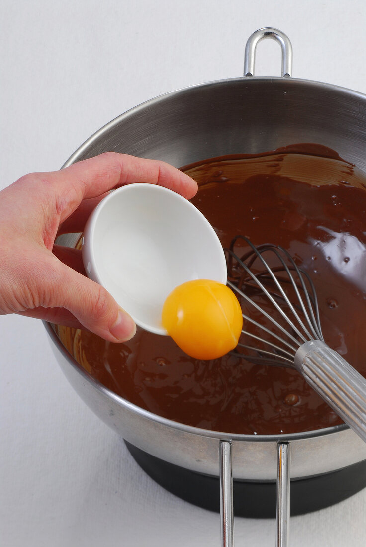 Egg yolk being added in melted chocolate in pan, step 3