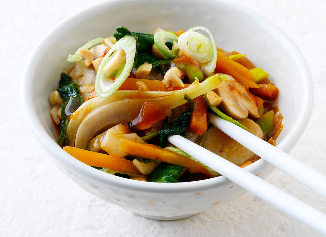 Stir-fried vegetables in white bowl with leeks, mushrooms and chopsticks
