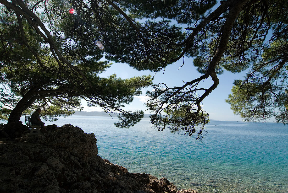 View of person sitting on bench at sea coast