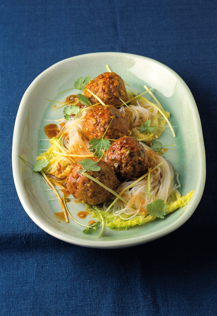 Four meatballs with noodles and cabbage on plate