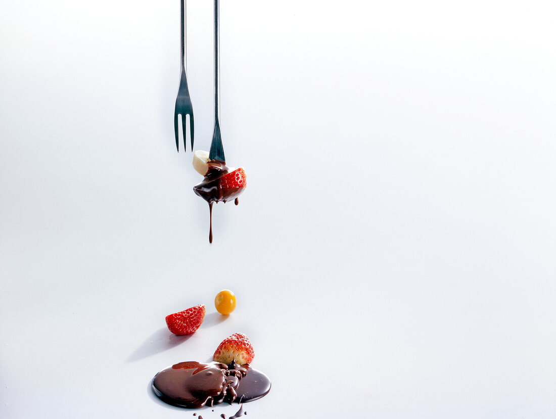 Close-up of banana and strawberry pieces dipped in chocolate sauce on white background