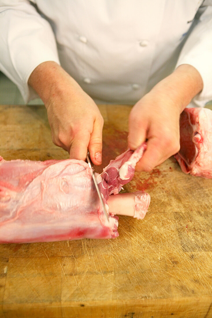 Chef cutting veal shank and separating tendon from the bone