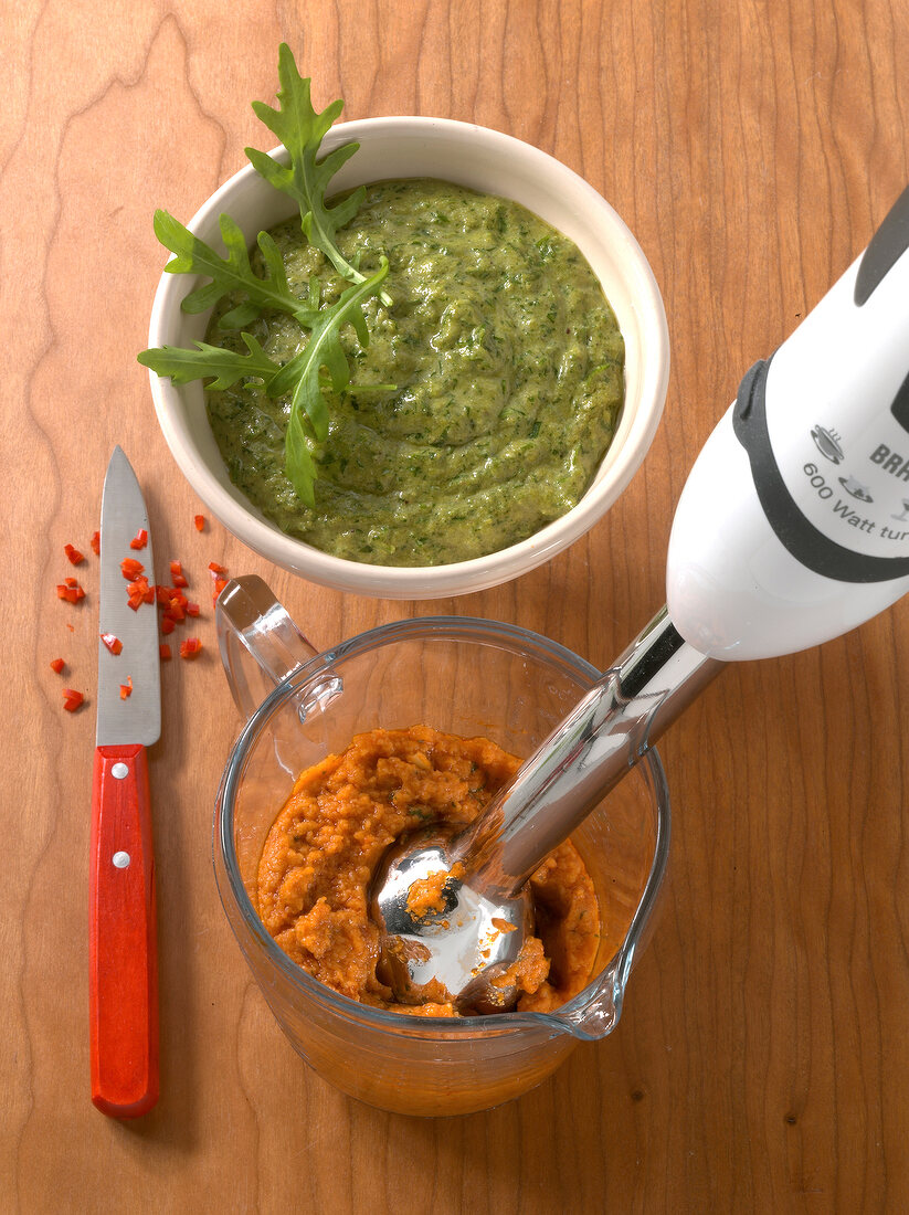 Rocket-stone mushroom pesto and spicy pesto rosso with hand blender in glass jar and bowl