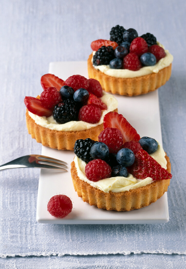 Three lemon berry tartlets with strawberries and blueberries on plate