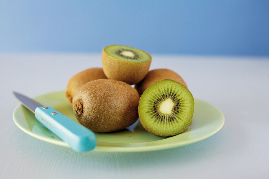 Close-up of whole kiwis, kiwi cut into half and knife on plate