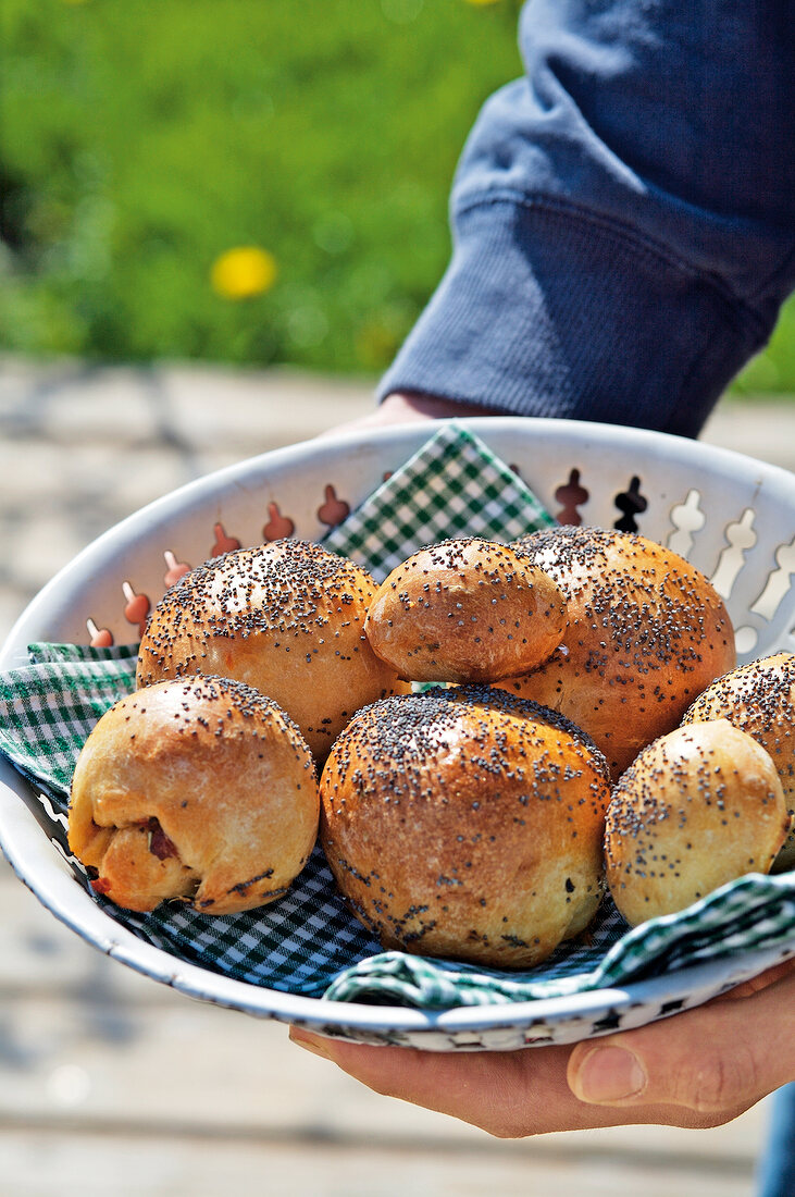 Close-up of man's hands holding bread basket with poppy seed roll 