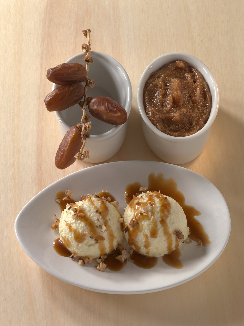 Two scoops of ice creams with caramel sauce and pesto date on wooden board