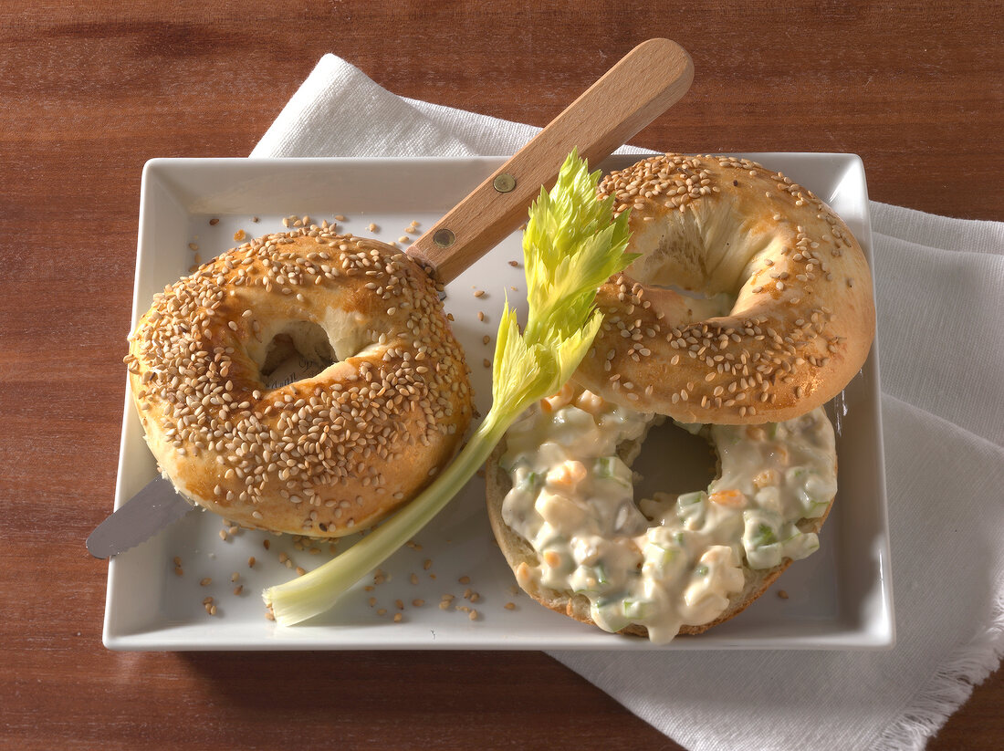 Two sesame bagel, one with egg salad and other being cut into half