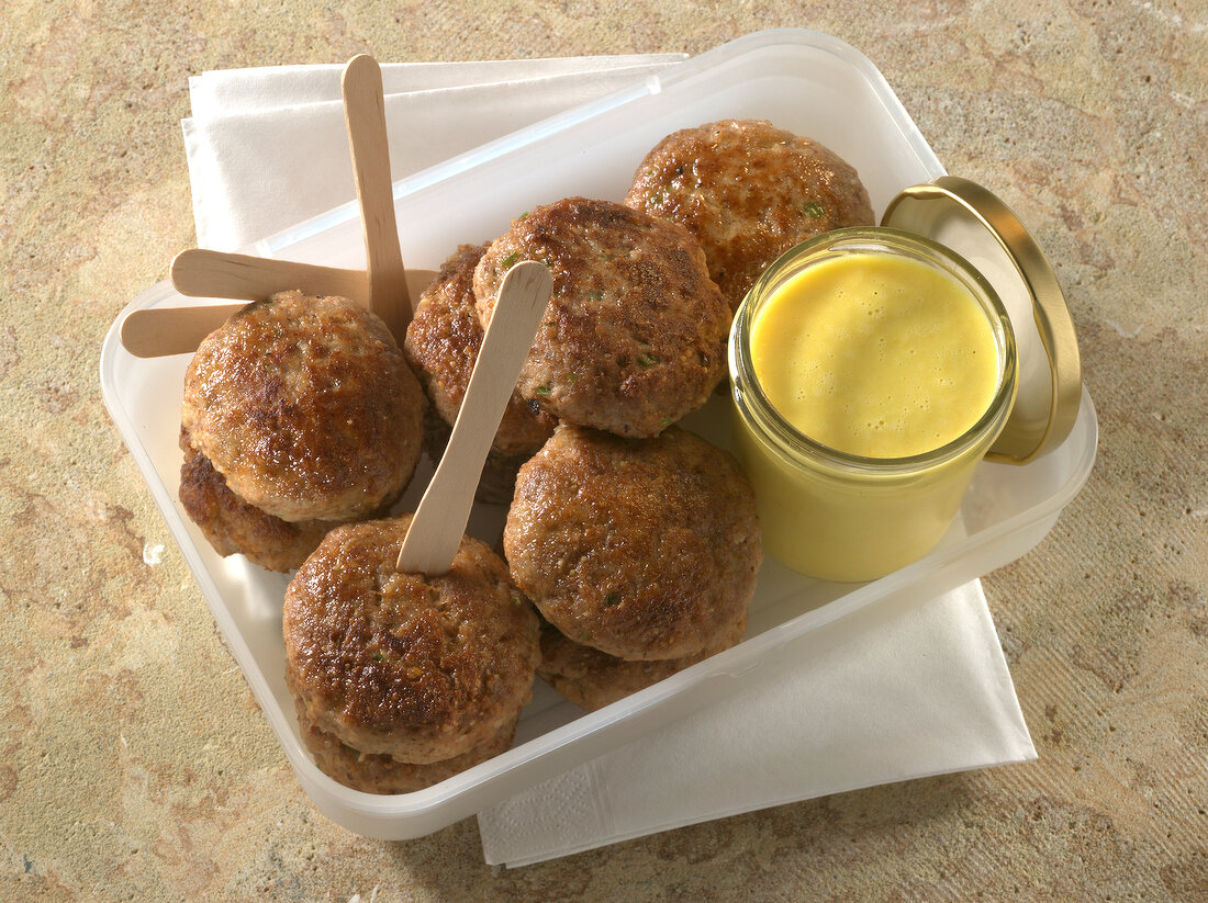 Chilli meatballs with pepper and bowl of coconut dip in plastic box