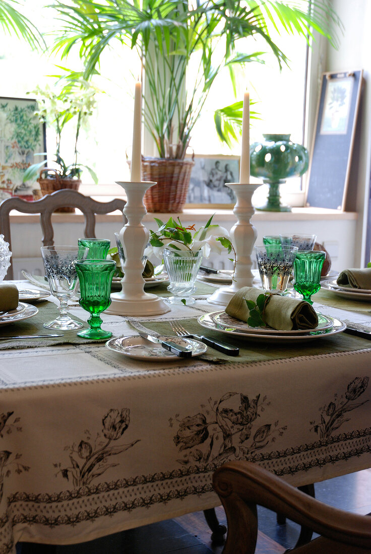 Two candles holder with green glasses, plates and cutlery on table
