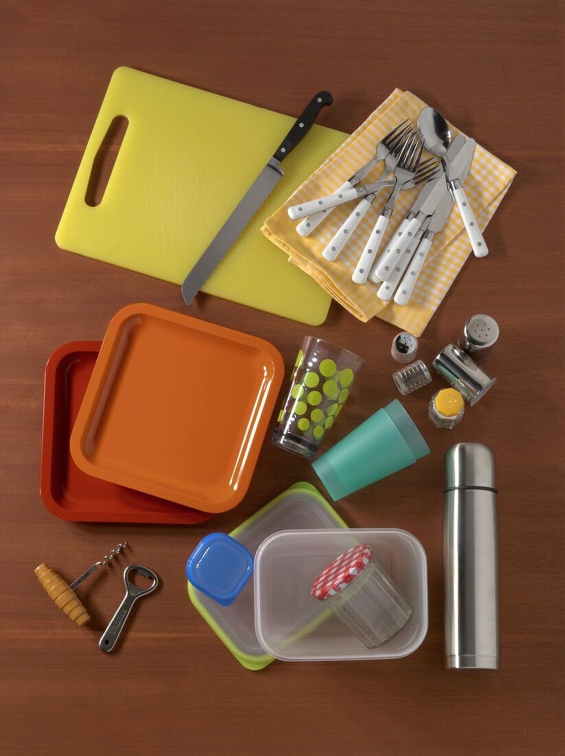 Chopping board, cutlery, plates, thermos bottle and cans on brown background