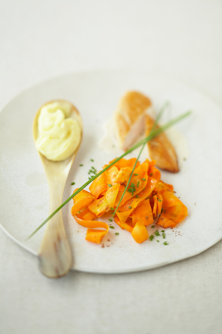 Caramelized carrots, chicken and chives on plate and creme fraiche on spoon
