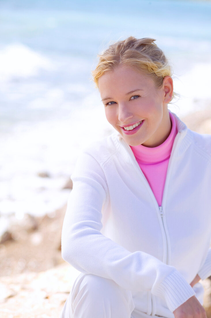 Beautiful blonde woman wearing white jacket and pink turtleneck t-shirt, smiling