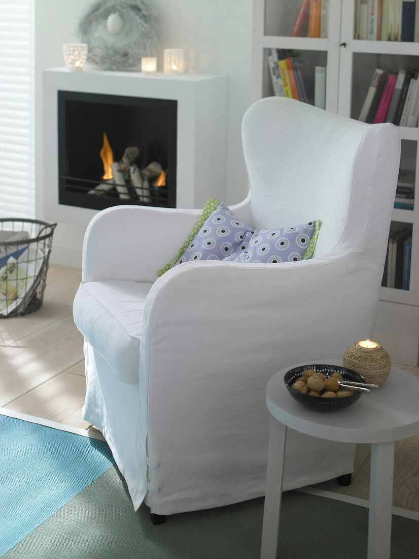 White wing chair in front of fireplace and book shelf