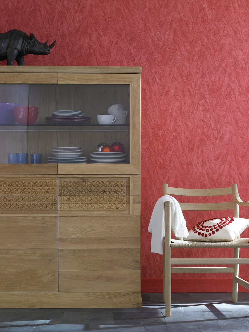 Wooden cabinets with carved ornaments and chair with cushion against red wall