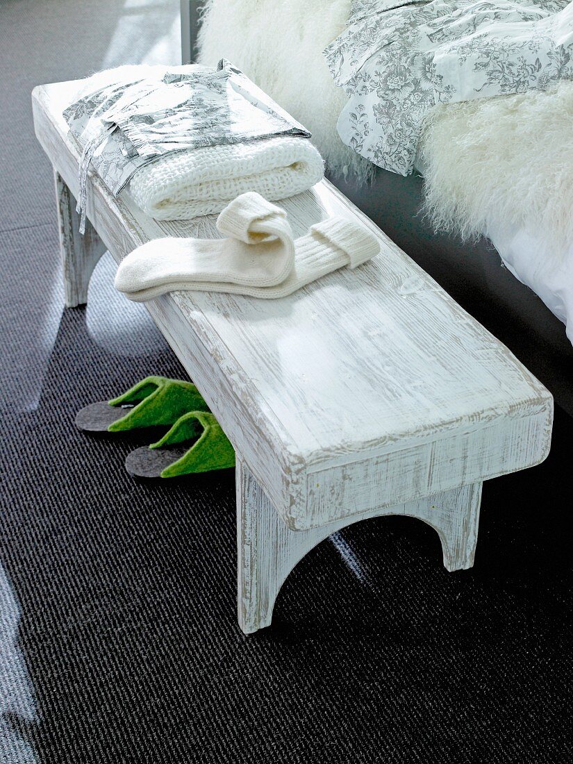 Rustic wooden bench beside bed with towel, socks and handkerchief