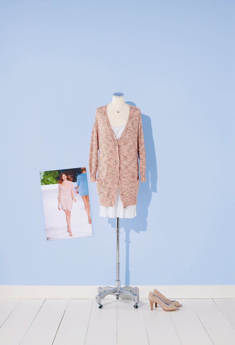 Sweater over white dress hanging on mannequin against blue background