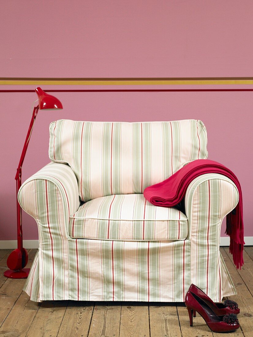 Armchair with striped cover and red metal standard lamp against pink wall