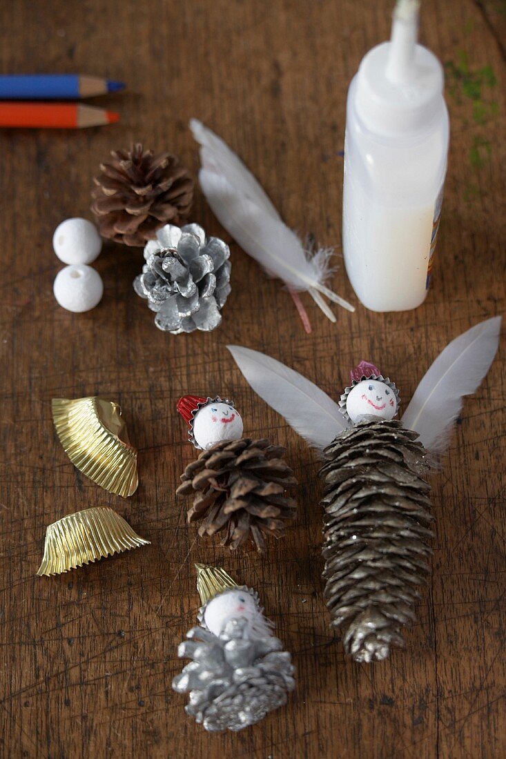 Weihnachtliches Bastelmaterial - Tannenzapfen, Federn, Klebstoff und Kugeln auf Holzablage